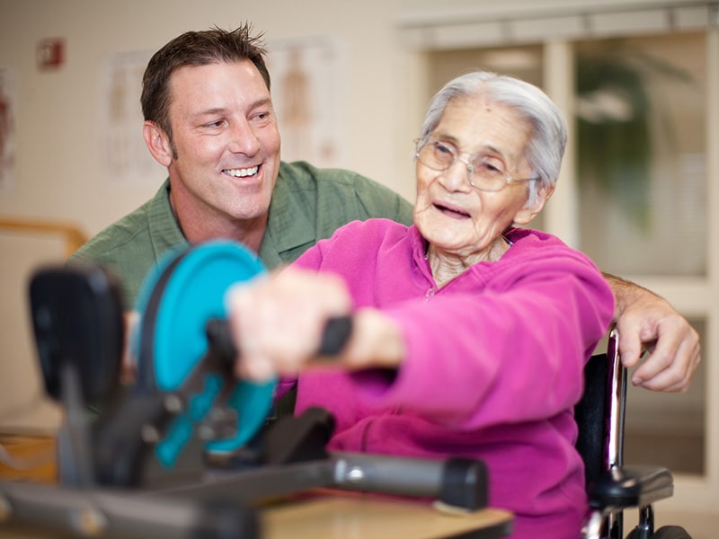 a rehab therapist helping an elderly woman with an arm exercise in the rehab gym