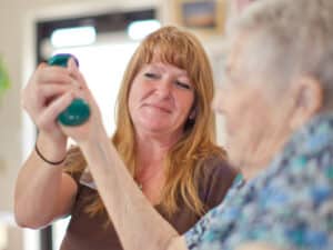 a rehab therapist helping an elderly woman lift a hand weight