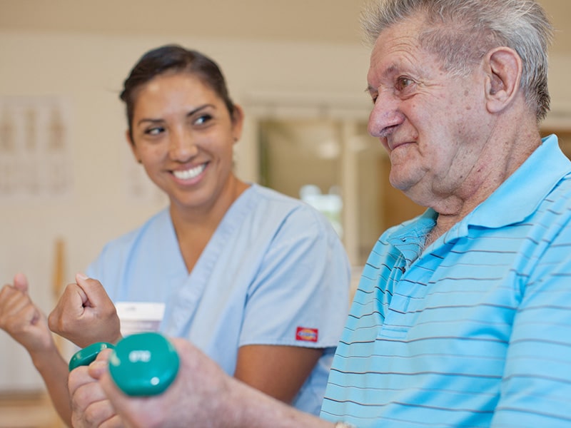 a rehab therapists helping an elderly man in the rehab gym